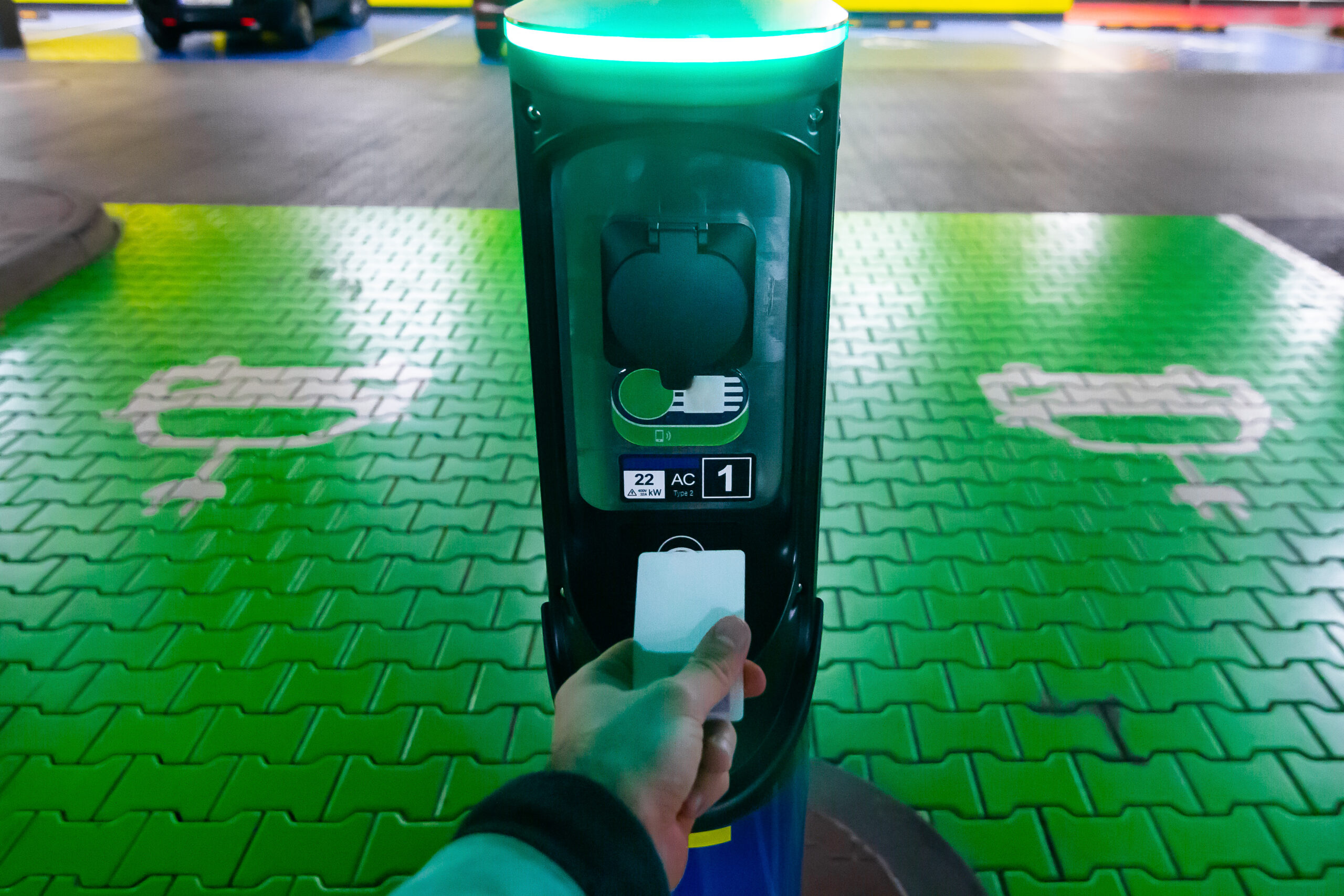A Man Pays For Charging An Electric Car. Hand Holding Catd To Pay At Charging Station. Concept Of Green Electricity, Clean Environment, Emission Reduction.